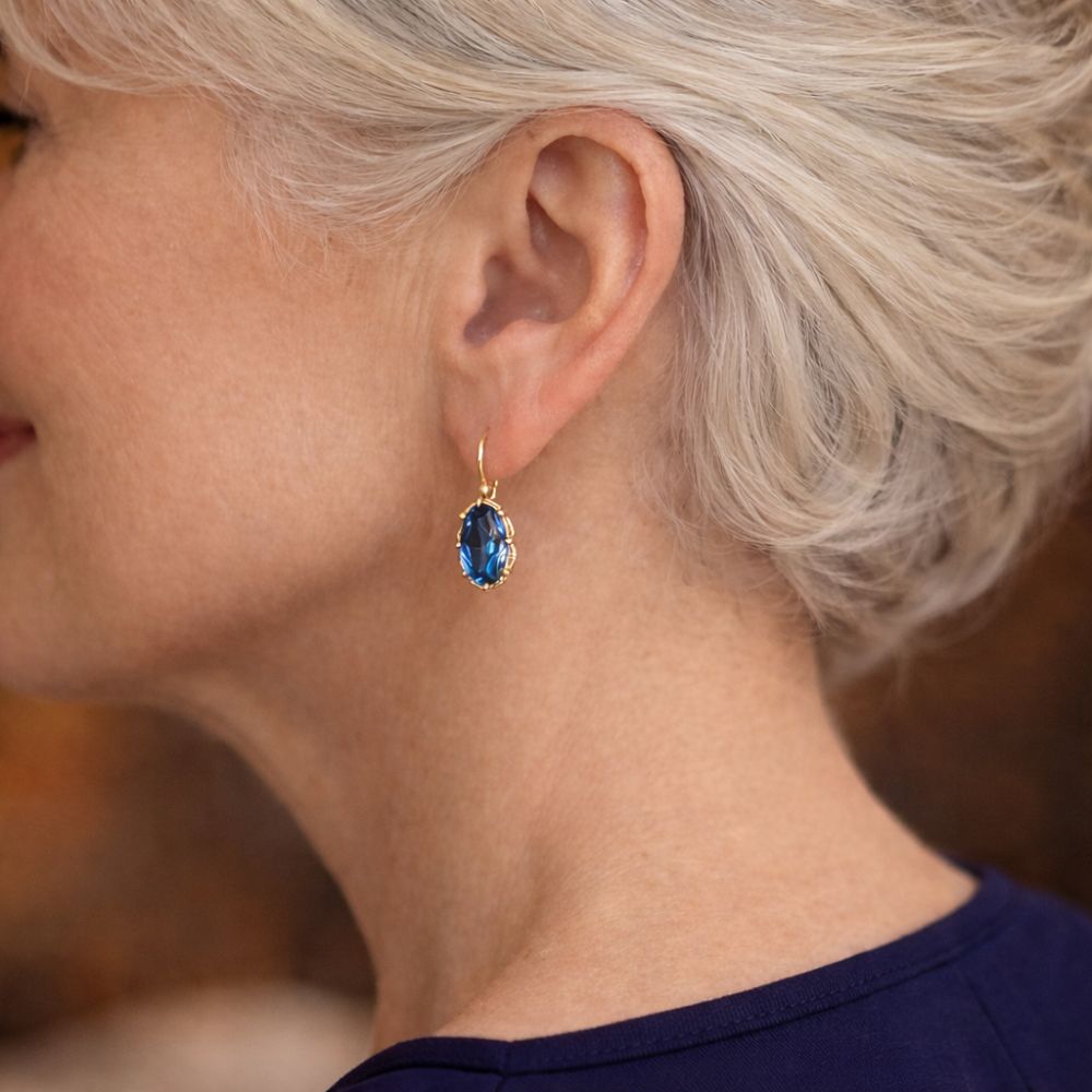 Aretes dorados con detalles en azul y florales, de la marca Rose & Oliver, mostrados en primer plano en la imagen.