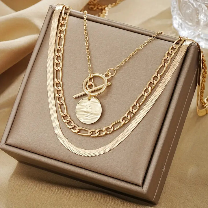 Gestapeltes goldenes Collier mit Münztextur, zeitgenössischer Stil, von der Marke Rose & Oliver, im Detail auf dem Bild.
