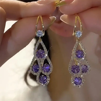 Brincos de gota com cristal roxo da Rose & Oliver, elegantes e brilhantes, pendurados em fio de metal prateado.